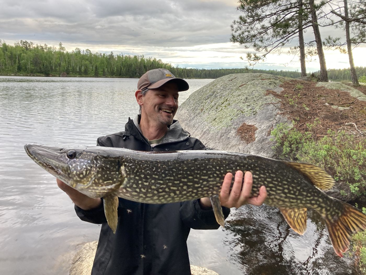 Matt Falcy holding a large northern pike at the edge of a lake.